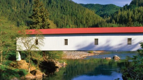 The red-roofed Milo Academy Covered Bridge reflects off the river.