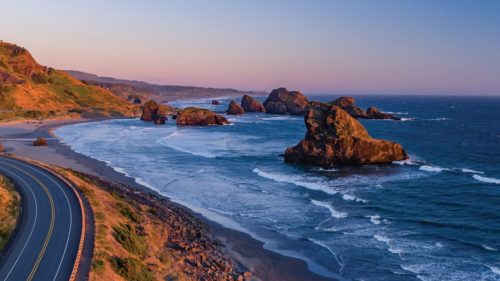 The Pacific Coast Scenic Byway hugs a mountain, giving passengers a view of massive rocks poking out of the ocean.