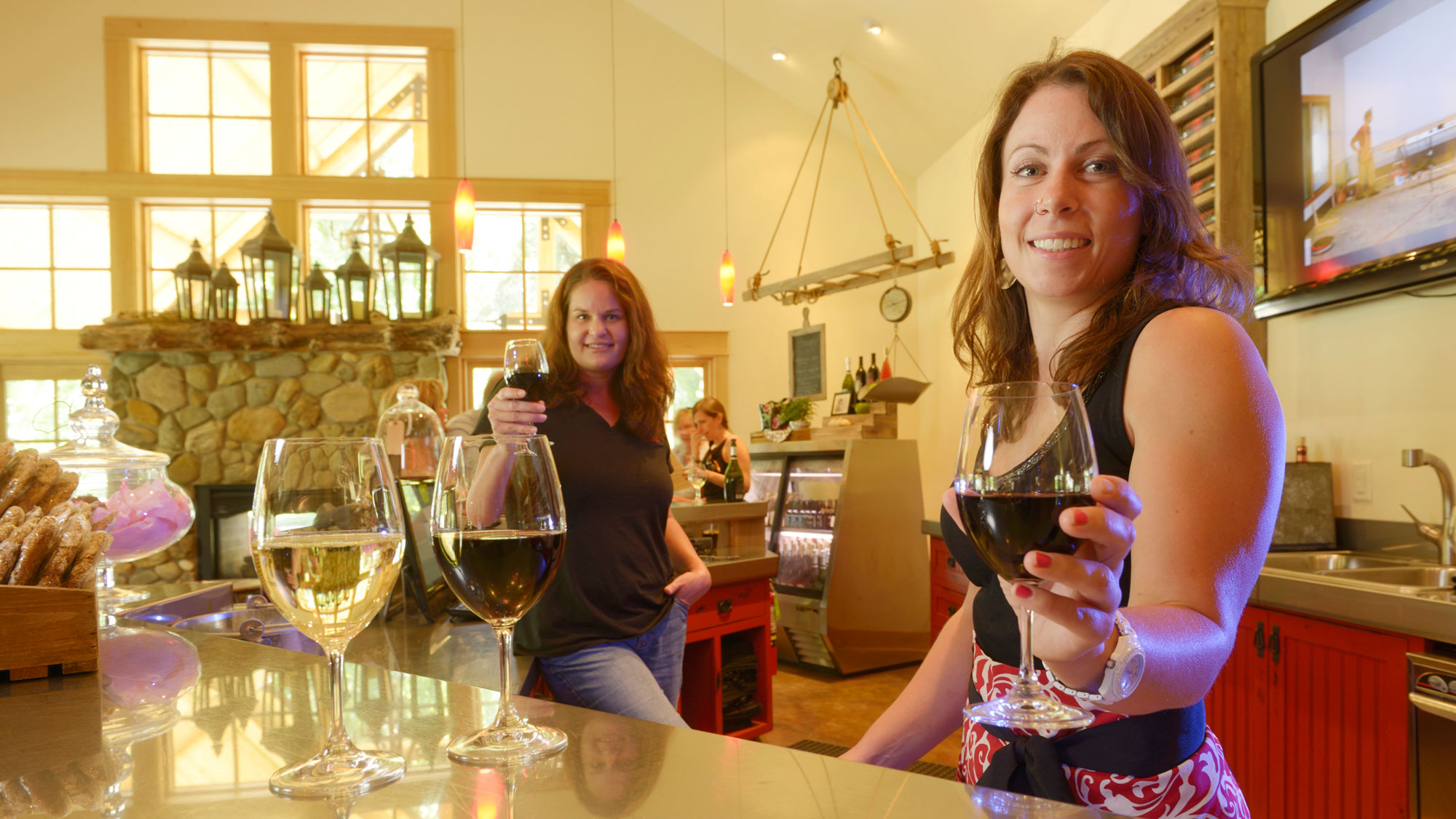 Female winemakers smile with glasses in cheers inside the charming tasting room of Red Lily Vineyards in Jacksonville, Oregon.