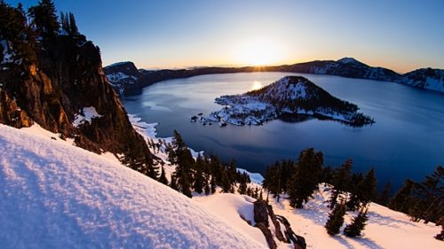 The rising sun lights up the snow and the water around Wizard Island. (Photography by Tyler Roemer)