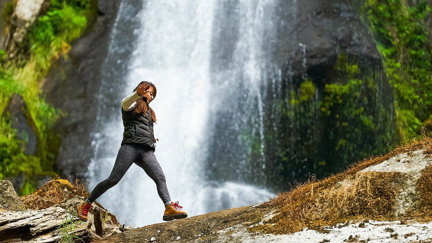 A girl walks in front of a waterfall.