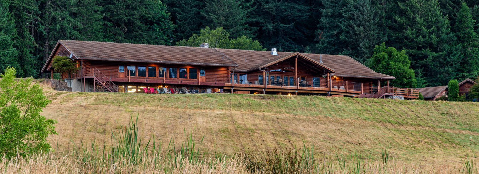A large wooden lodge sits on top of a grassy hill