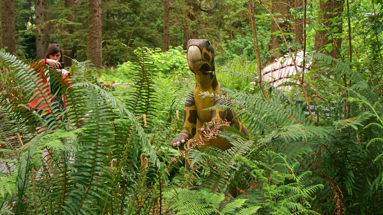 An outdoor dinosaur statue tucked into ferns