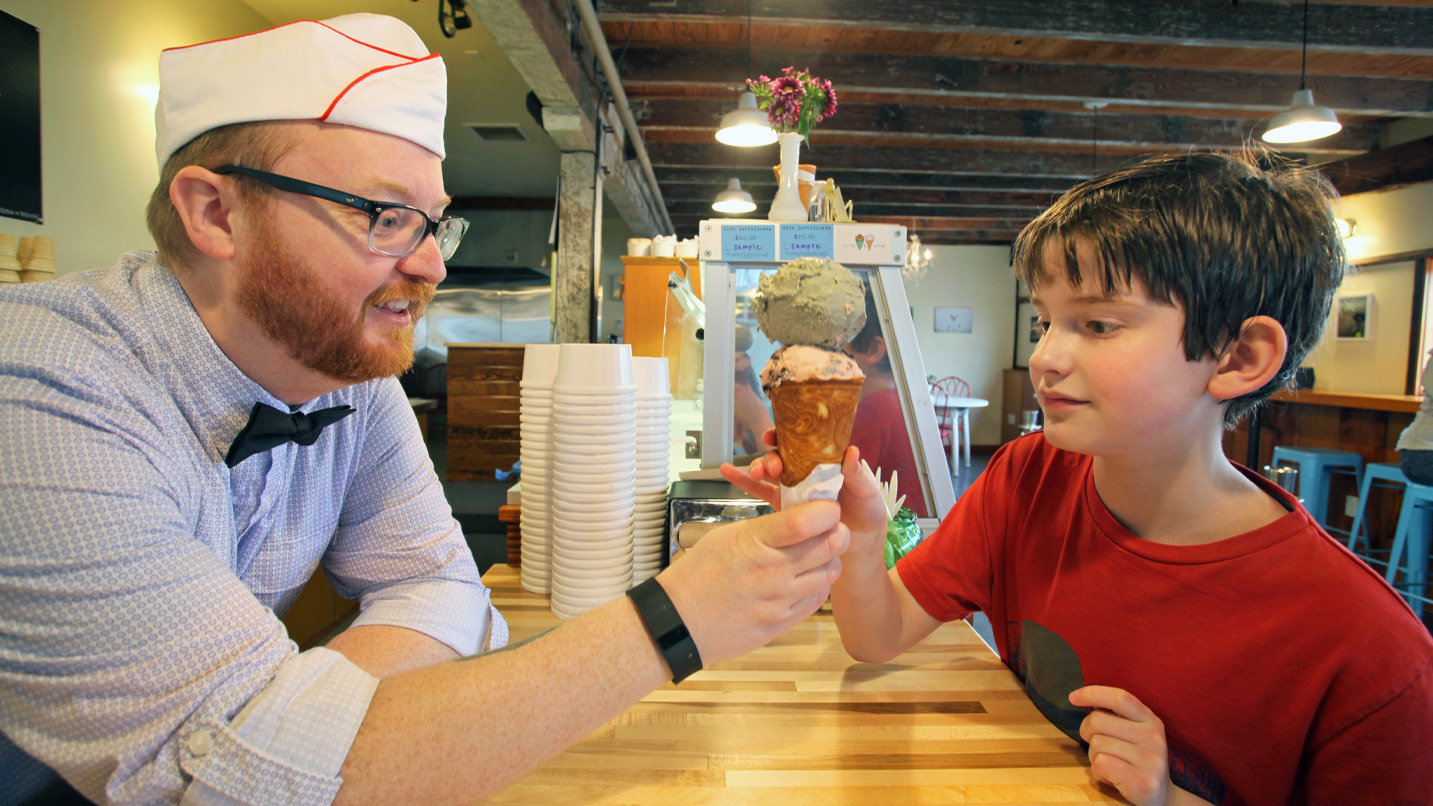 man with hat handing double scoop of ice cream to boy
