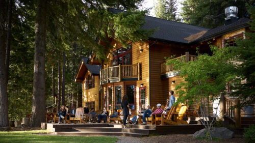 People sit on a wooden deck in front of a two story lodge