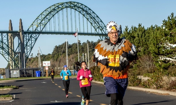 Man wearing turkey costume running in front of Yaquina Bay Bridge