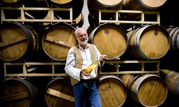 Clear Creek founder Steve McCarthy holding a pear bottle in front of barrels
