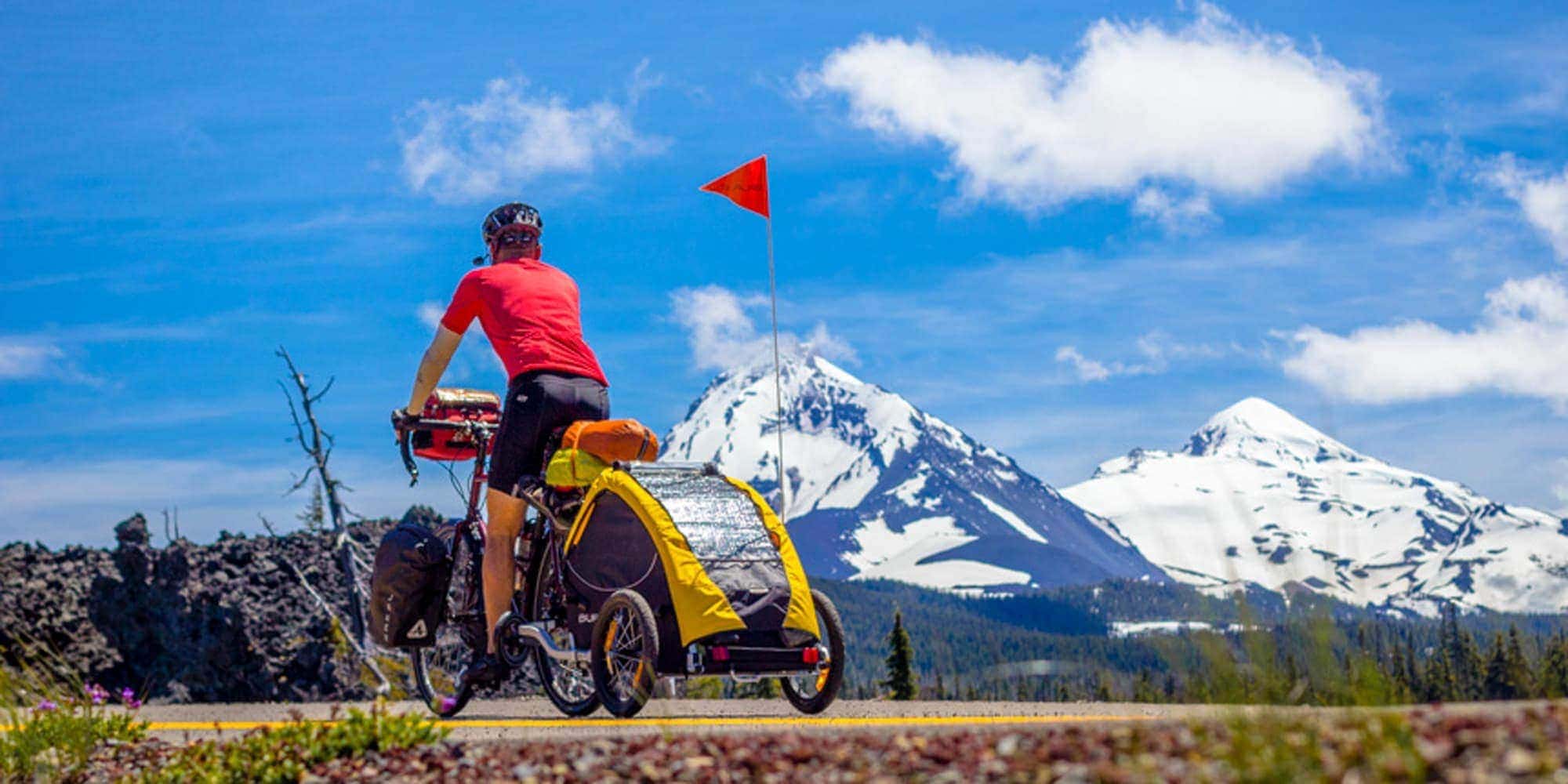 Cyclist towing dog trailer with snowy mountains in background