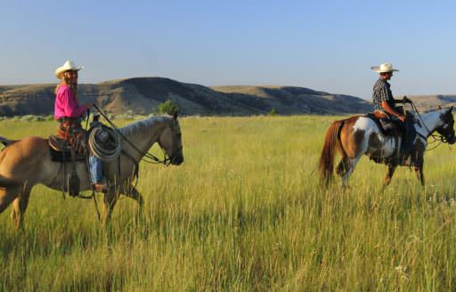 Cowboy and cowgirl ride through grassland at Wilson Ranches Retreat.