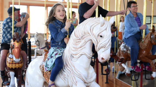 A young girl rides on a white horse carousel figure