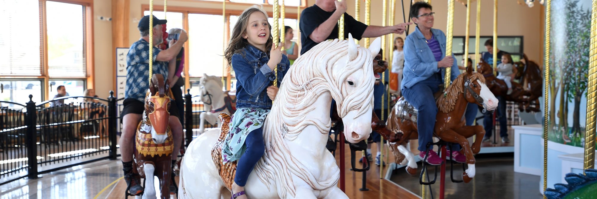 A young girl rides on a white horse carousel figure