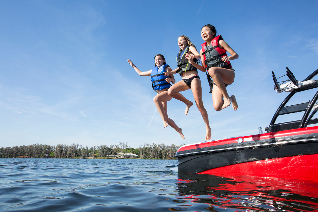 three girls wear life vests and jump from boat into water