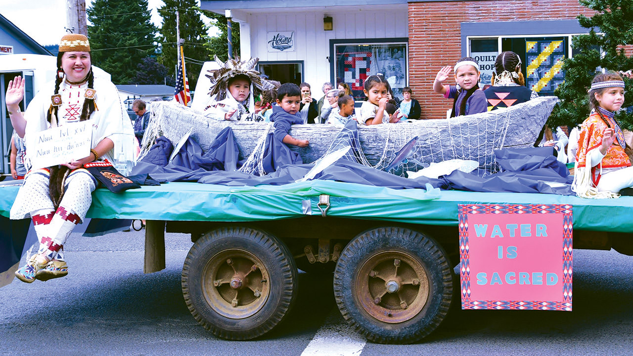 Young members of the Siletz Tribe site on a parade trailer that says, "water is sacred."