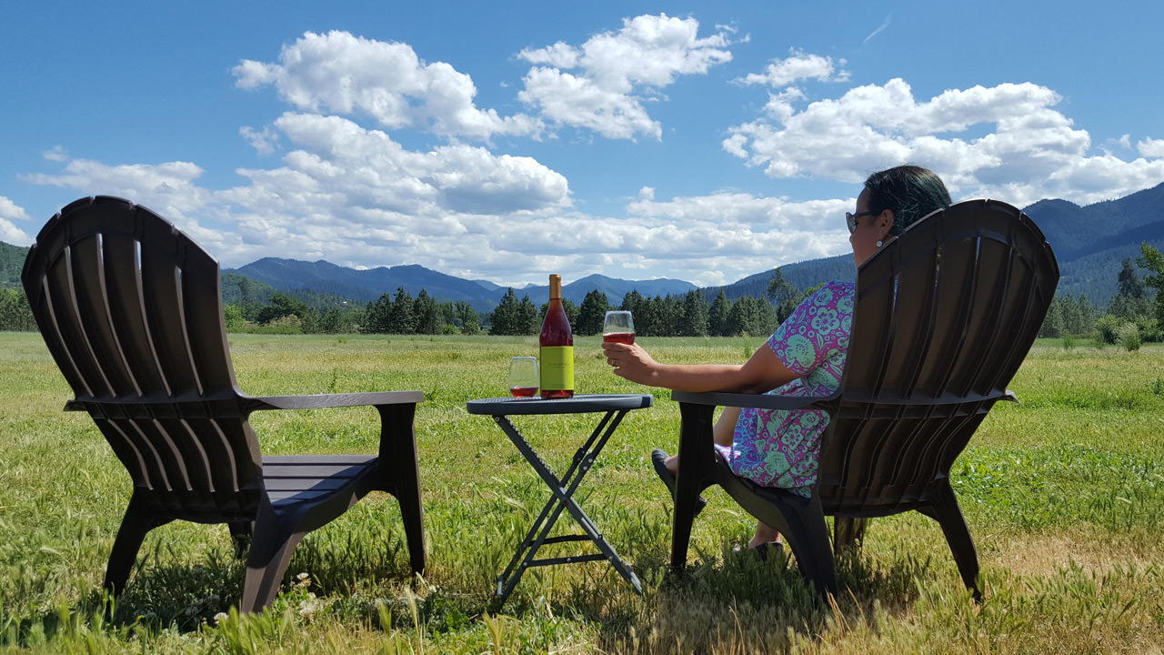 A person sips wine in a wooden lawn chair.
