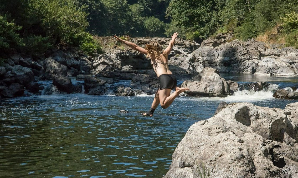 A girl jumps into a pool of water from a rock.