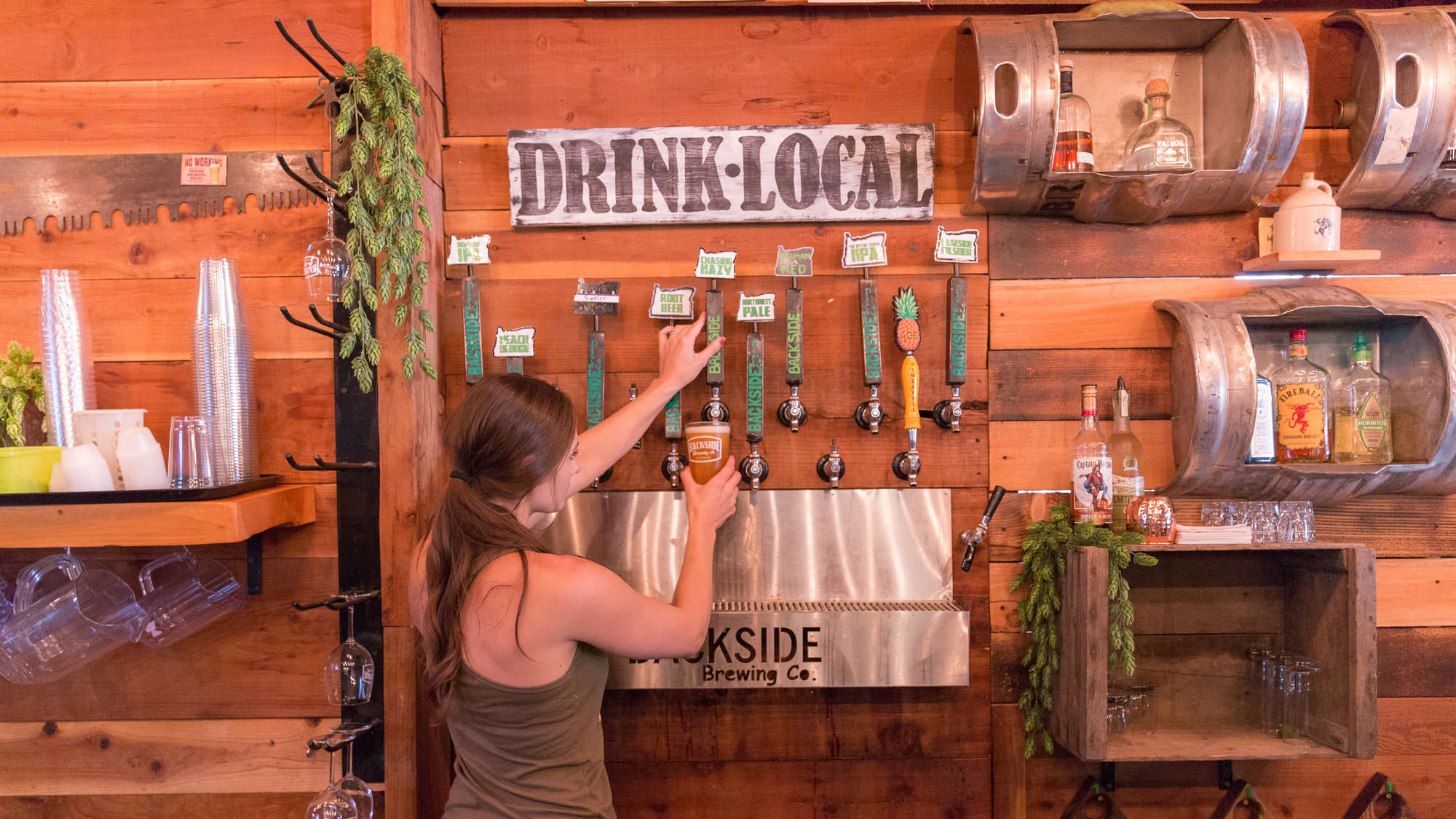 A bartender pours beer under a "drink local" sign at Backside Brewing, one of the stops on the Great Umpqua Food Trail.