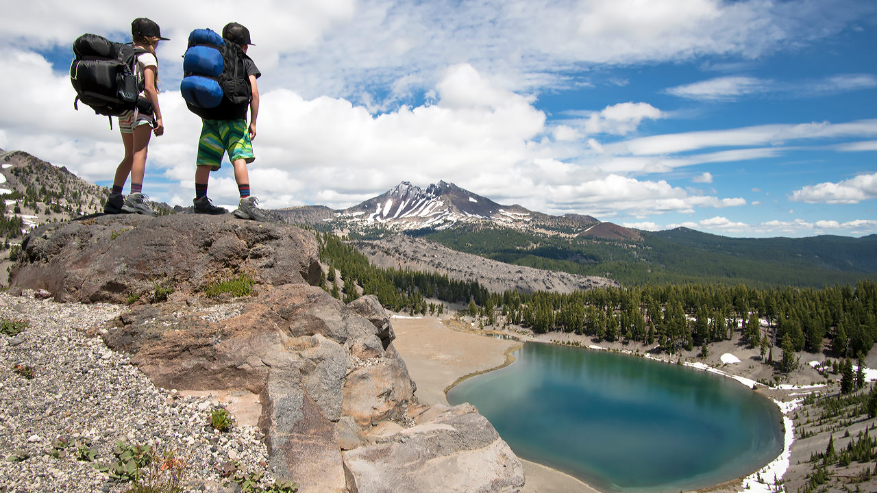 Two kids wearing camping backpacks look over Moraine Lake.