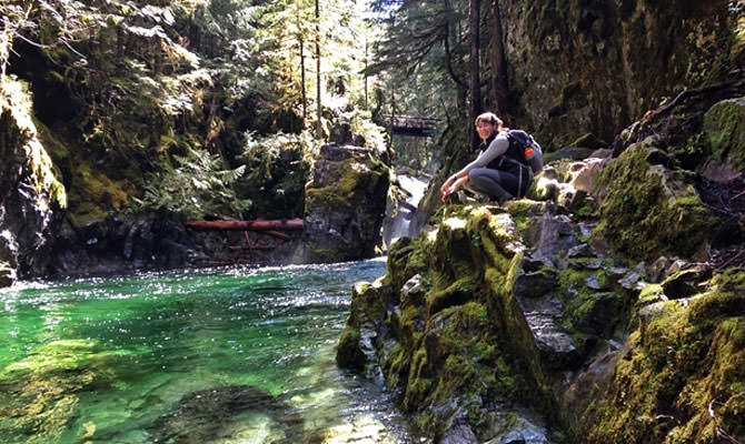A hiker looks over a blue-green pool of water.