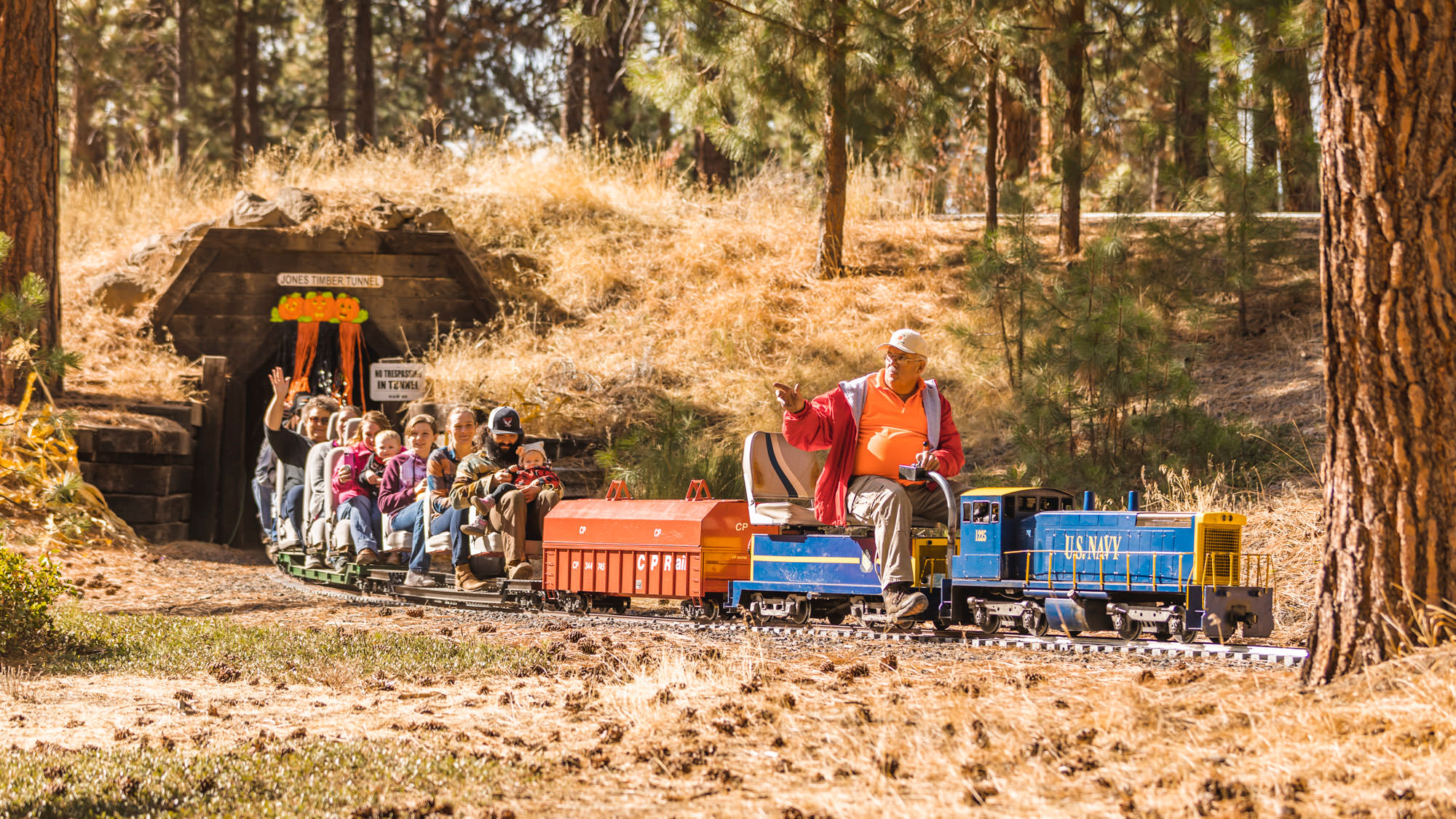 People smile and wave as they sit atop miniature train compartments after leaving a tunnel.