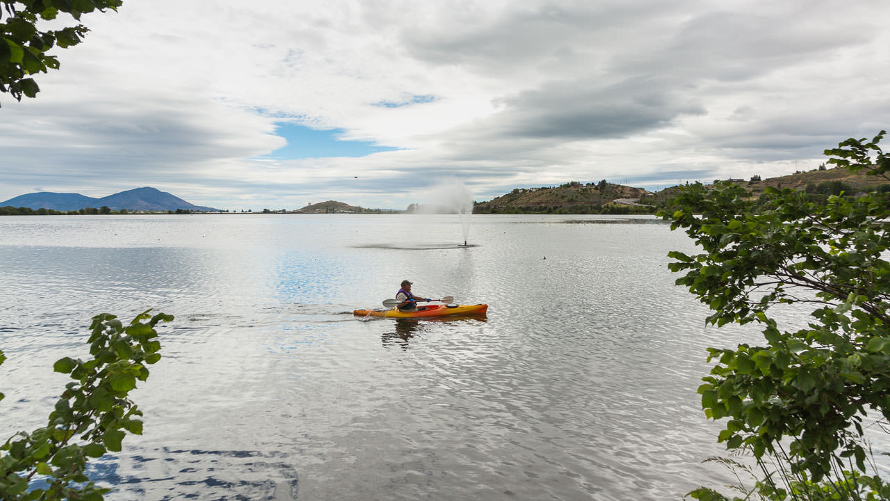 A man paddles a kayak in a vast lake.