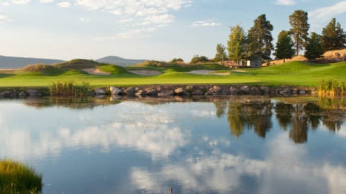 A pond reflects the sky, with a green golf course in the background.