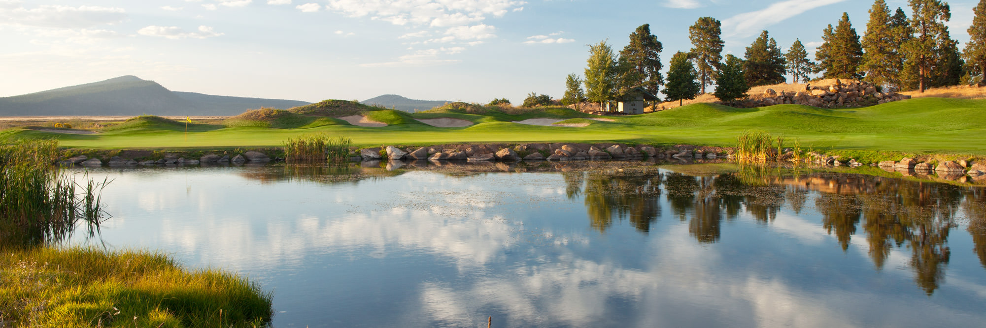 A pond reflects the sky, with a green golf course in the background.
