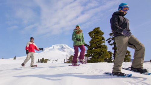 Three brightly covered snowshoers smile with Mt. Hood's snowy peak in the background.