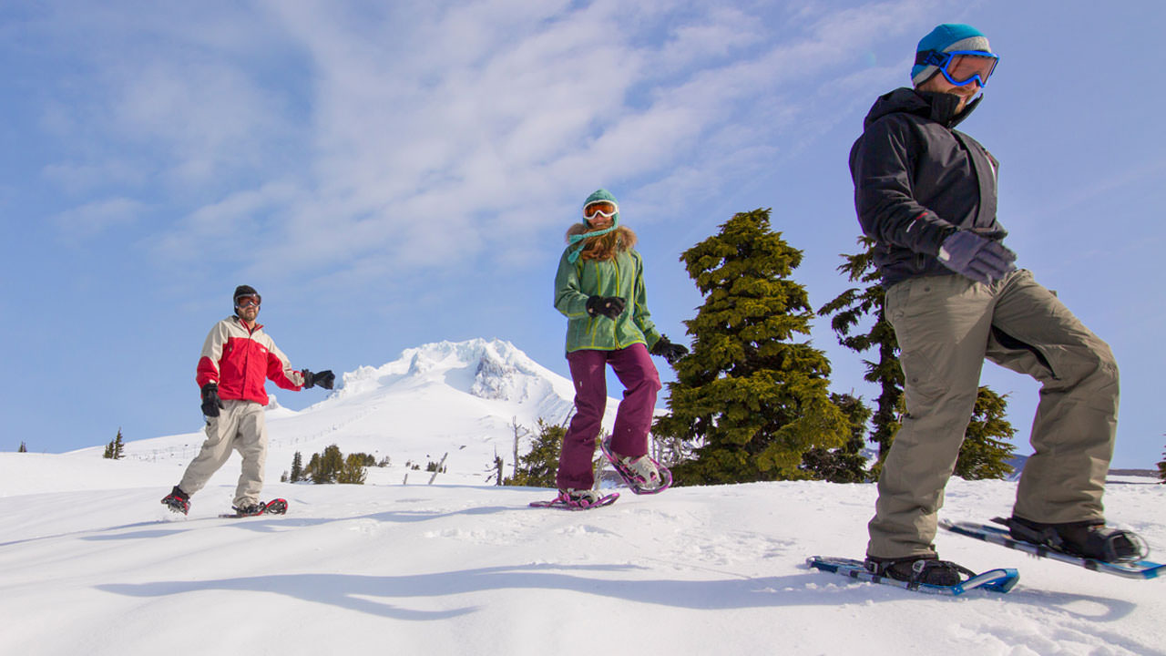 Three brightly covered snowshoers smile with Mt. Hood's snowy peak in the background.
