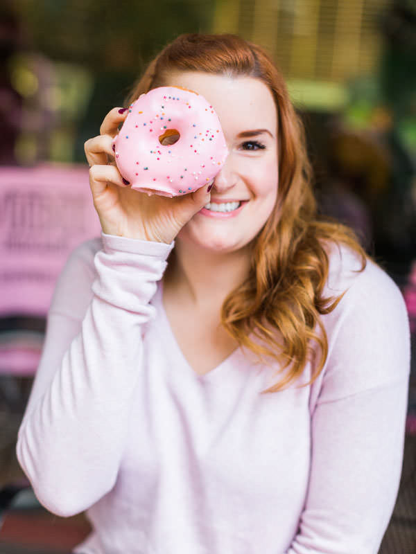A girl holds a pink frosted doughnut in front of her eye.