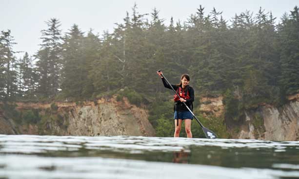 A girl paddleboards in an ocean cove.