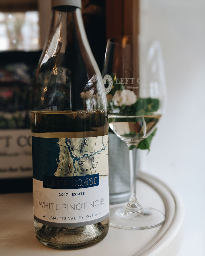 A bottle of white pinor noir with an uniquely Oregon label sits in front a glass filled to its quarter.