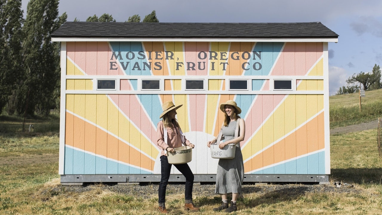 two people holding baskets in front of shed with colorful sunburst painted on exterior