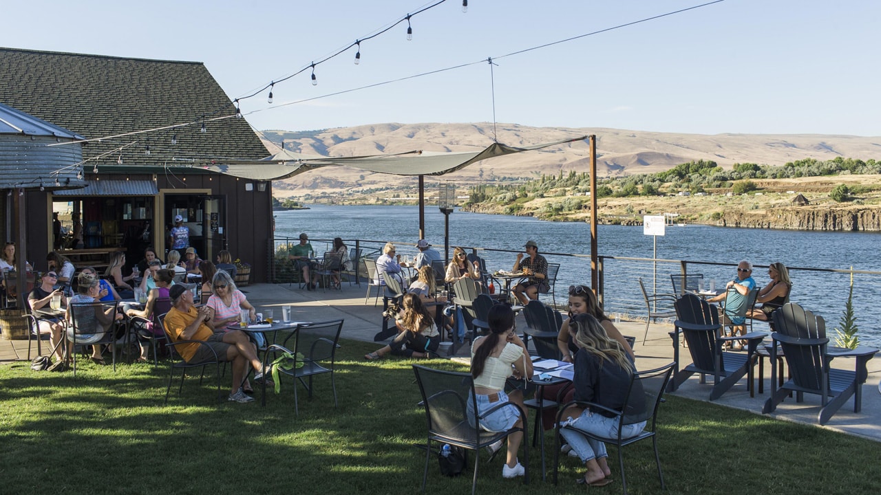 people dining outside in grassy area with river view in background