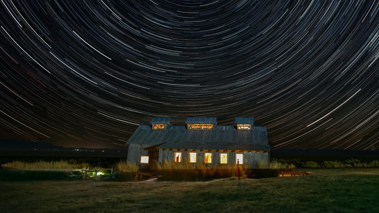 star trails at a lit-up cabin at night