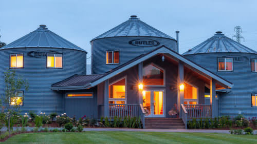 Renovated grain silos at Abbey Road Farm converted into stylish overnight accommodations, warmly lit at dusk with landscaped grounds in front.