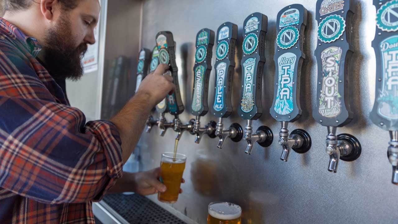 A bearded man pours beer from the tap.