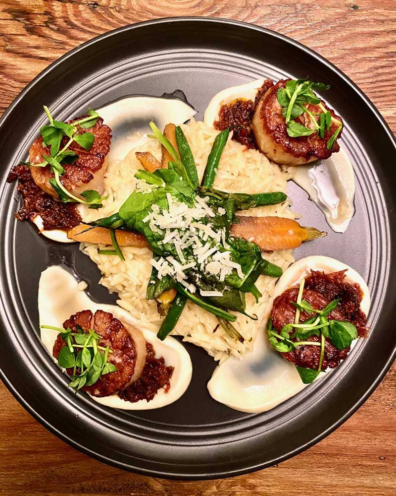 Four scallops are topped with bacon, herbs and white sauce.