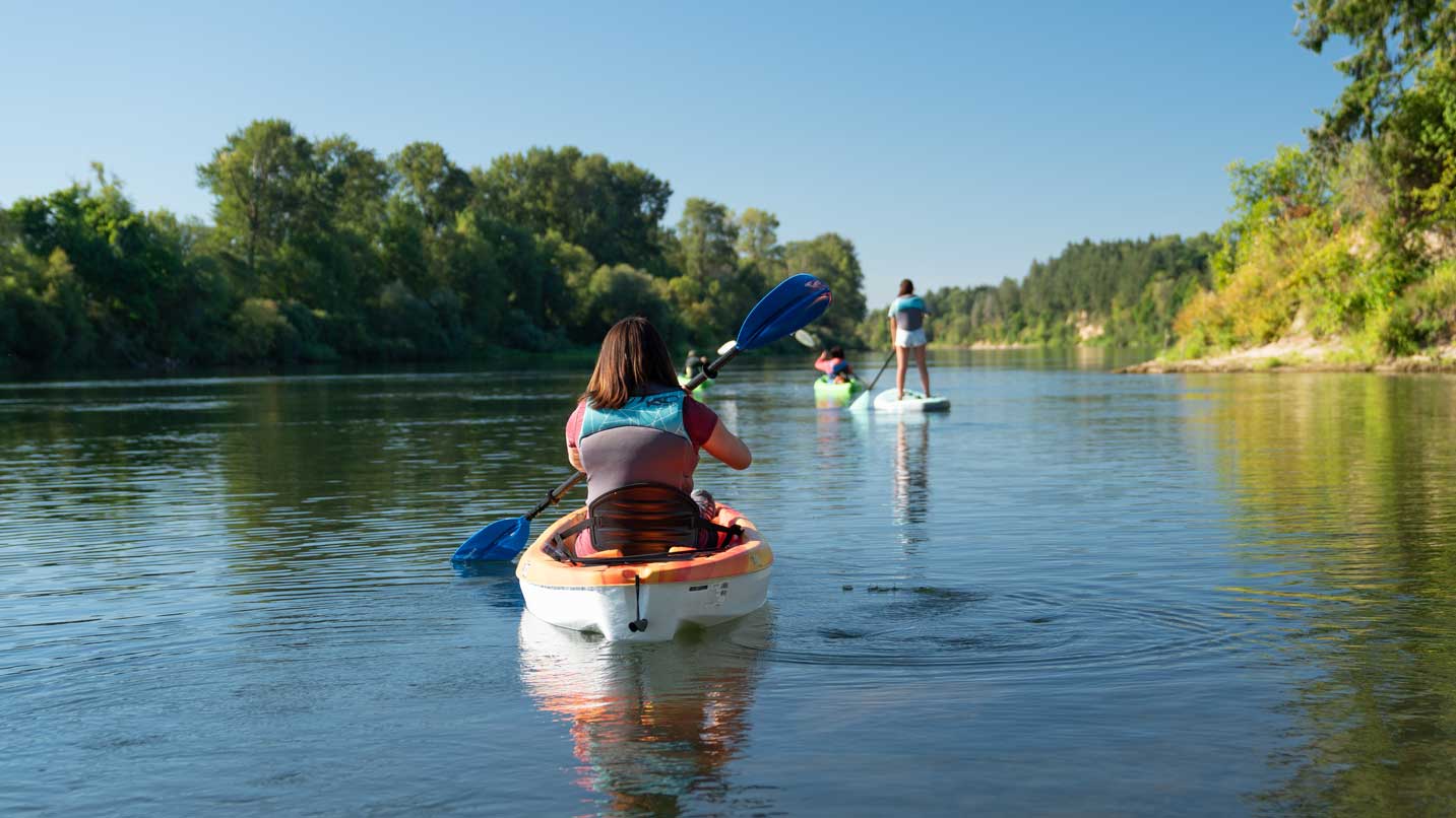 A kayaker paddles behind a stand-up paddleboarder on the Willamette River.