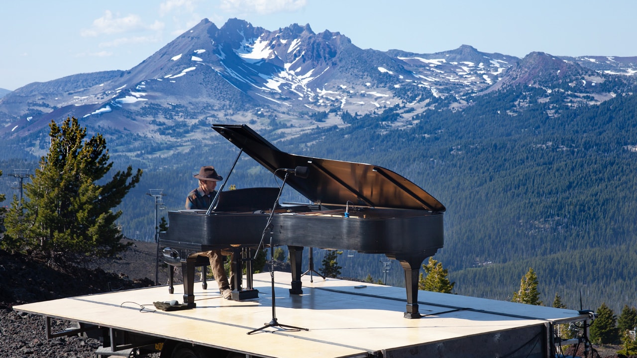 man sits at piano with mountains in background