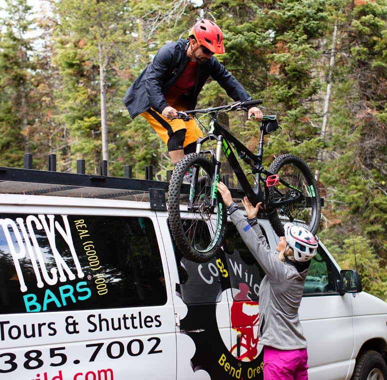 Two cyclists unloading mountain bikes from top of van