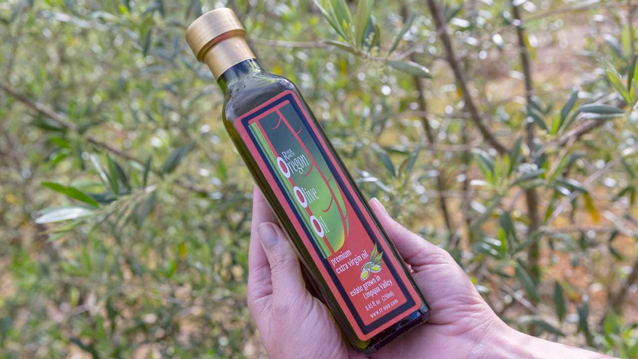 Two hands hold a bottle of olive oil in a orchard.