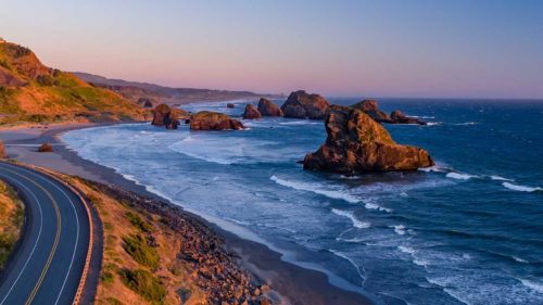 A bird's-eye view of the Pacific Coast Scenic Byway as it winds around a corner to a view of rock formations on the shore.