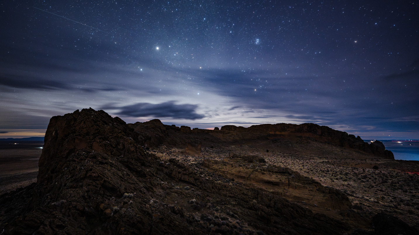 Starry dark skies over a monolith rock in the desert.