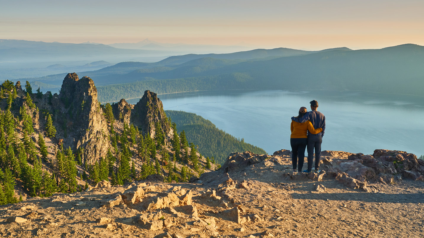 Two people high on a cliff overlooking a caldera.
