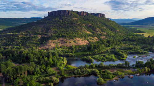 A volcanic plateau stands tall above green trees and a blue river.