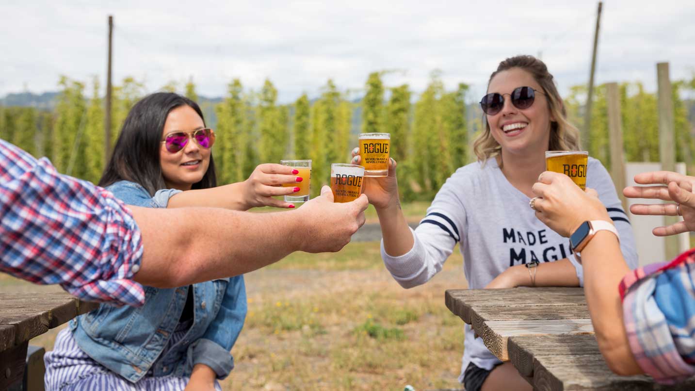 Four friends cheers their beers in front of a hop field.