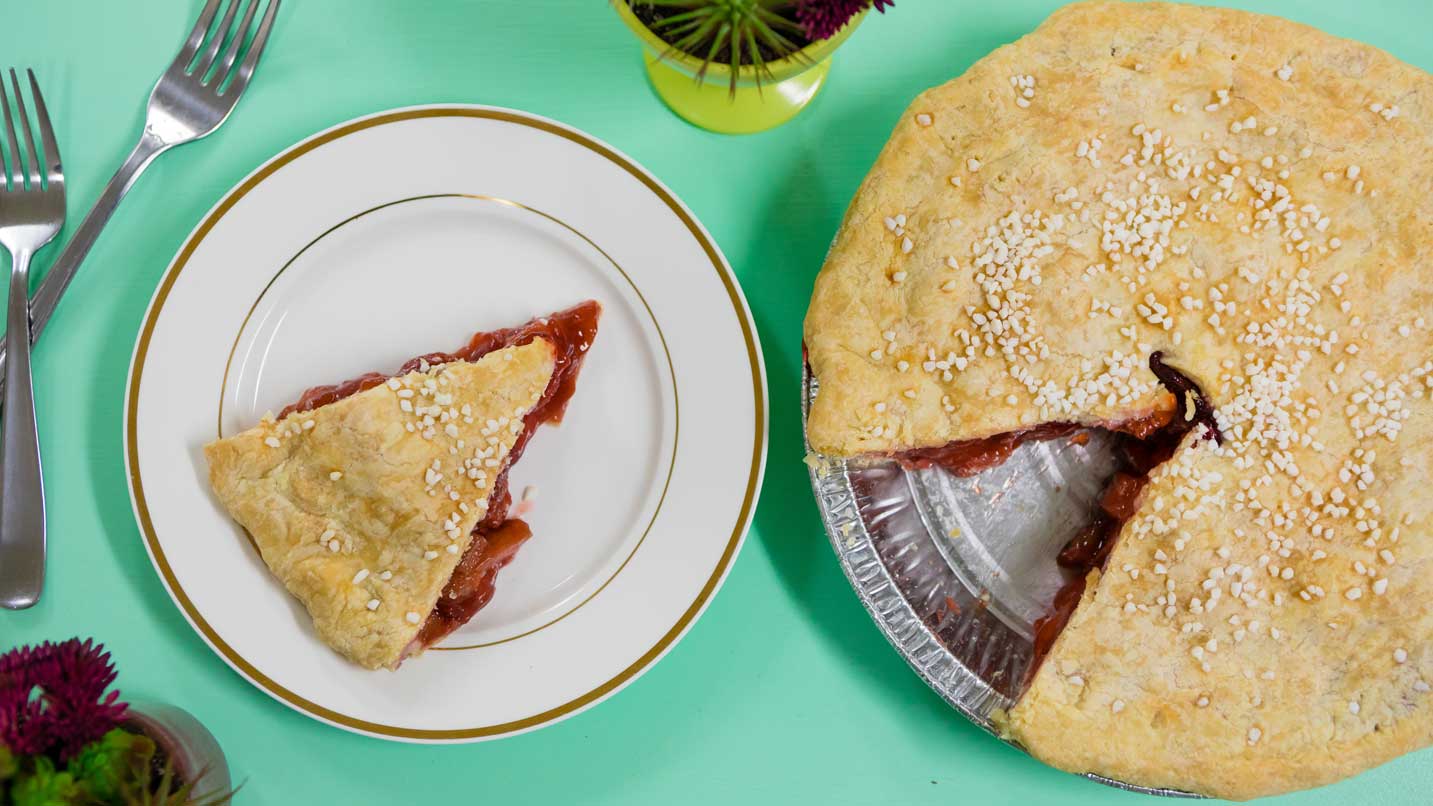 A slice of berry pie sits on a plate next to the rest of the pie.
