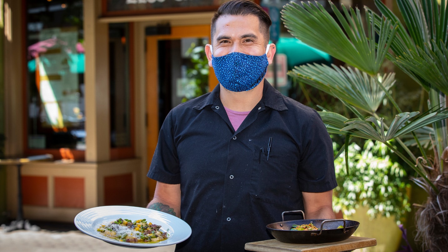 A waiter smiles behind a face covering.