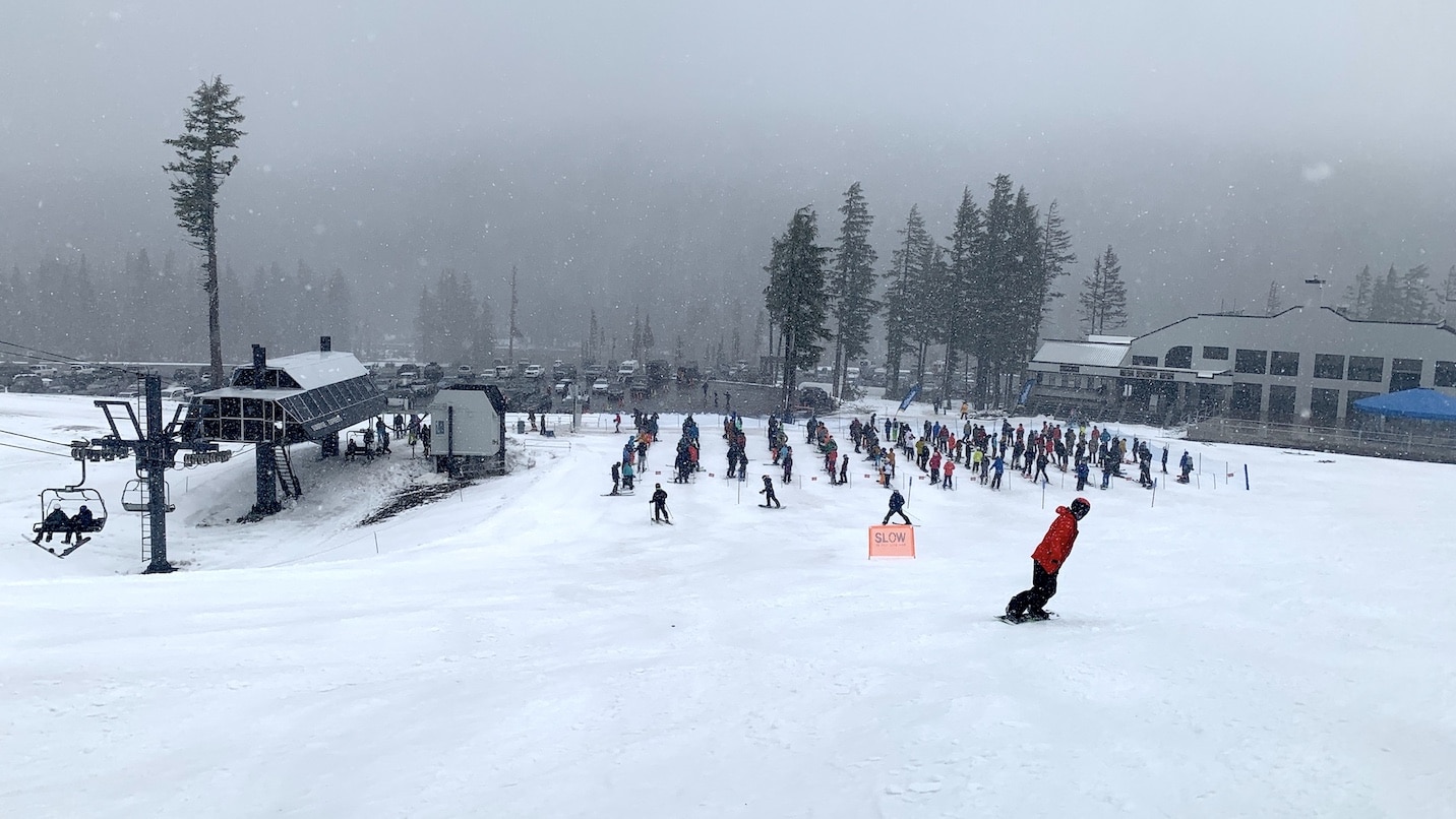 People waiting to ski are spaced out in lines.