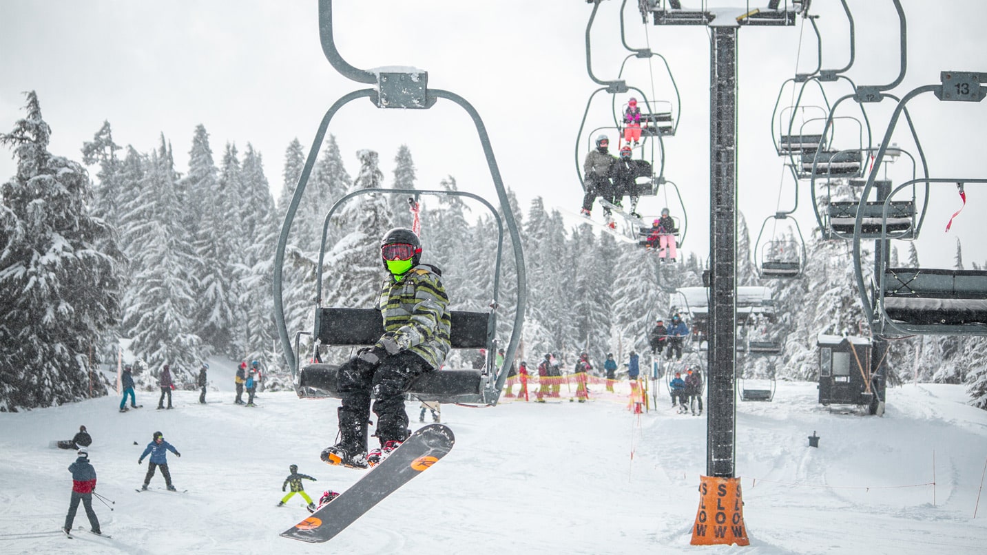 A snowboarder wears a mask while riding a lift.